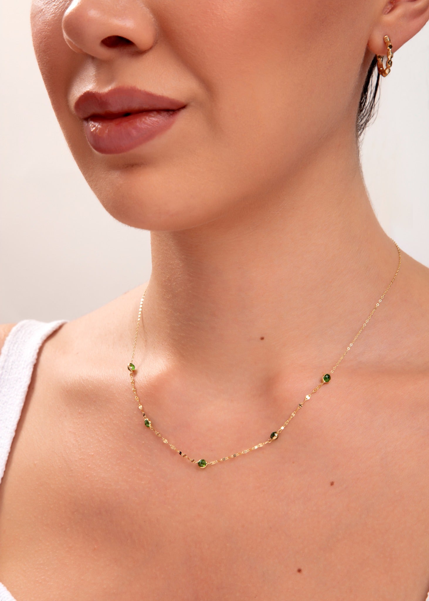 Model wearing gold necklace with green gemstones

