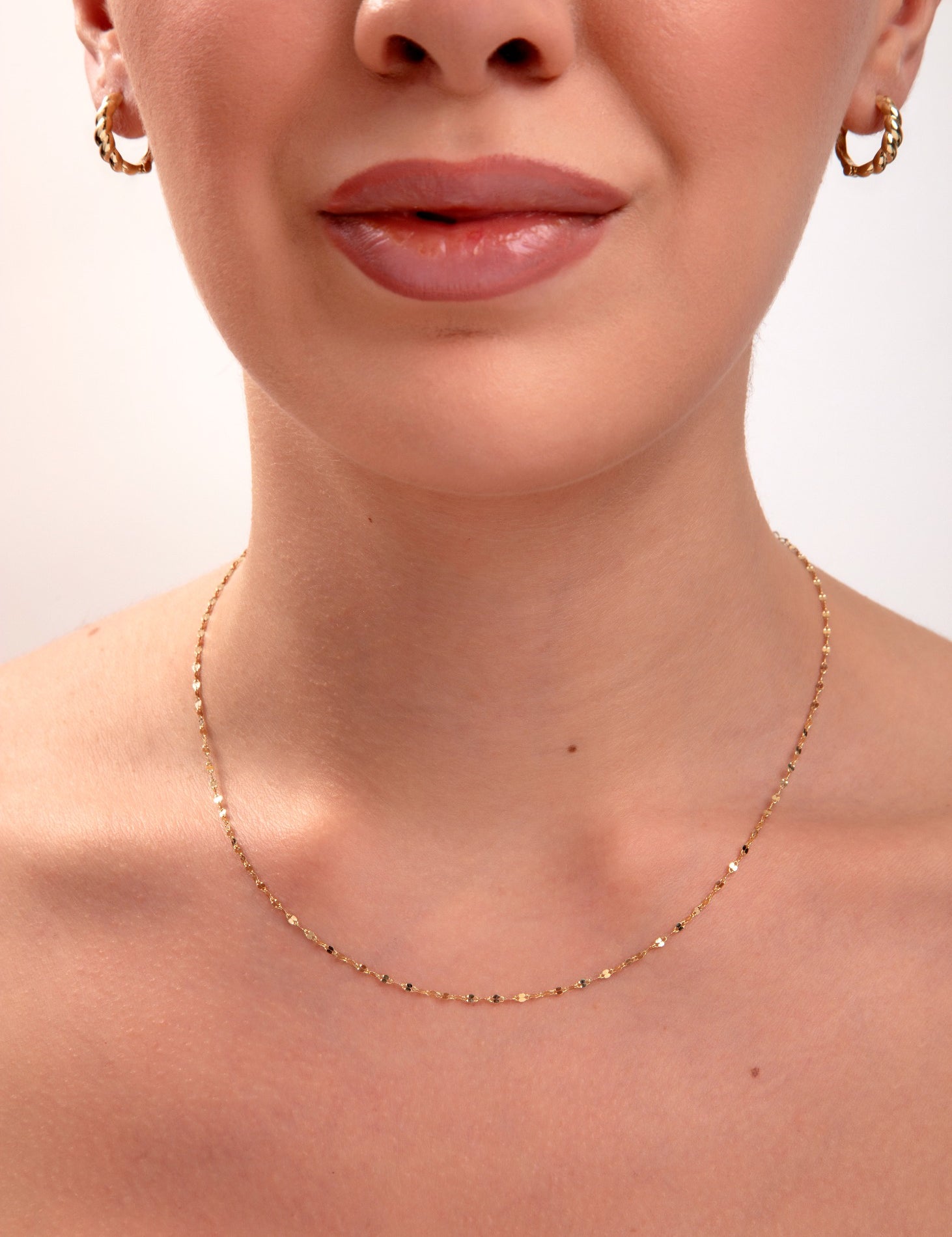 Gold faceted disc chain necklace on model's neck, minimalist jewelry with light-catching sparkle

