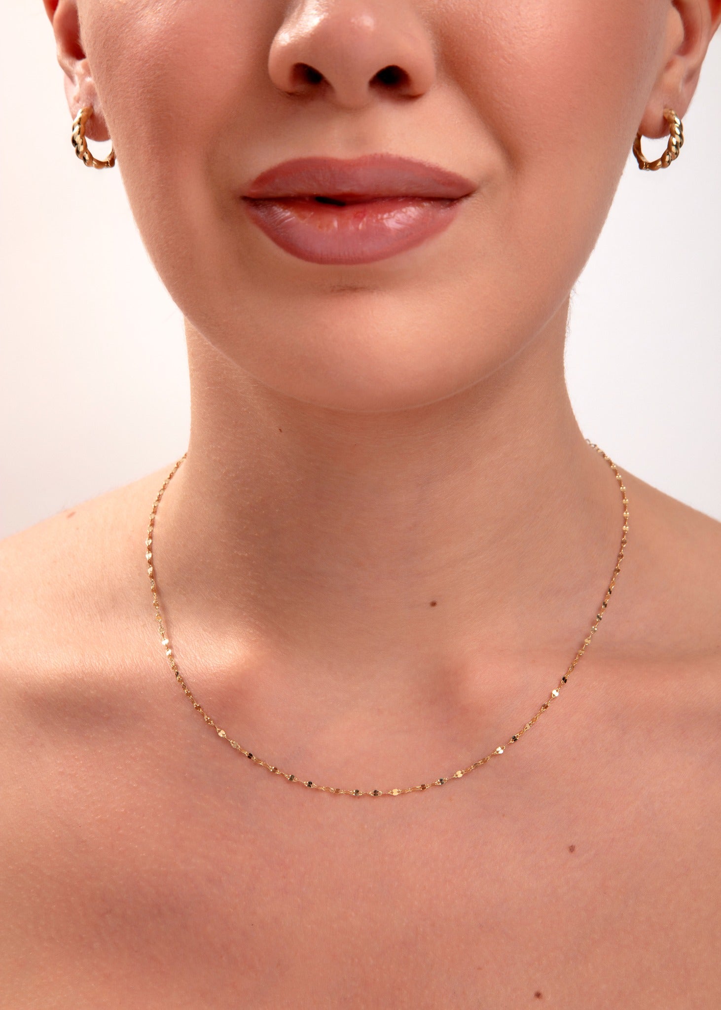 Gold faceted disc chain necklace on model's neck, minimalist jewelry with light-catching sparkle

