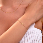 Gold clover charm bracelet with faceted chain on woman's wrist, matching necklace visible, elegant minimalist jewelry

