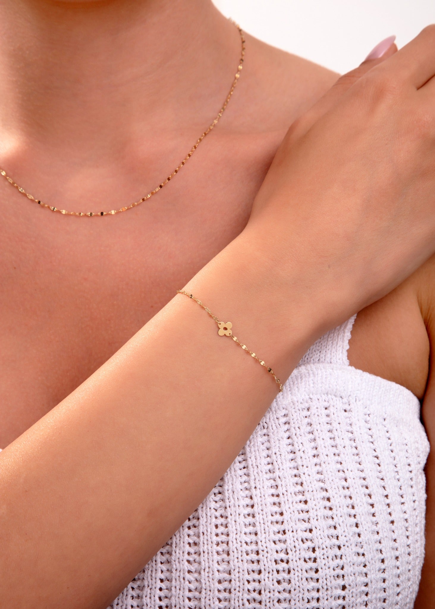 Gold clover charm bracelet with faceted chain on woman's wrist, matching necklace visible, elegant minimalist jewelry

