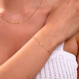 Gold flower charm bracelet with faceted chain on woman's wrist, matching necklace visible, elegant minimalist jewelry


