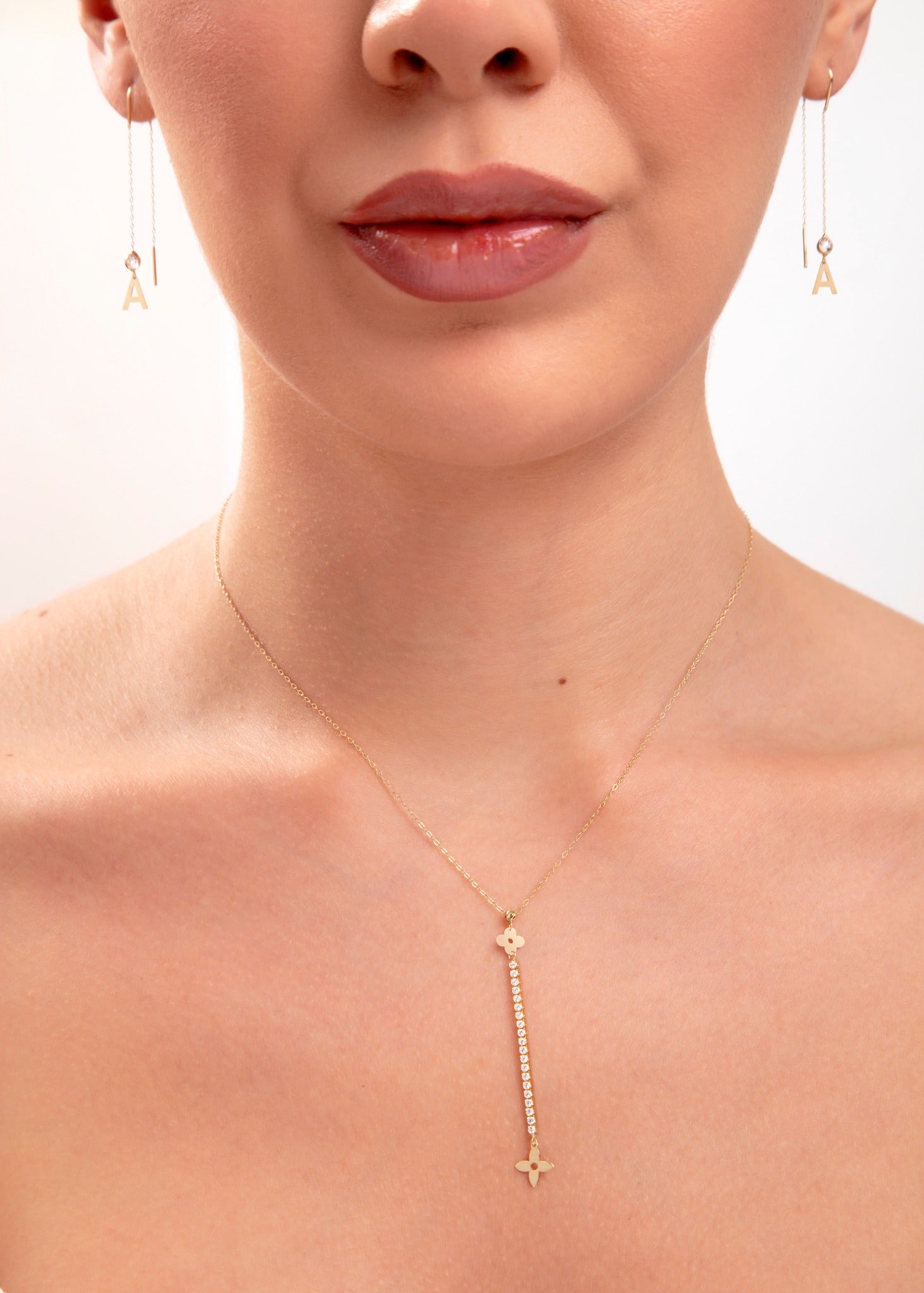Woman wearing 14K gold plated floral drop necklace with crystal bar and initial threader earrings, model shows the letter "A"

