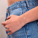 Delicate gold bracelet with four-leaf clover charm and crystal detail, worn on wrist, styled with blue denim jeans

