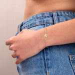 Minimal gold bracelet with four-leaf clover charm and crystal chain on wrist, styled with denim and white knit top

