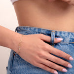 Close-up of a 14K gold plated lotus charm bracelet with crystal beads, worn with denim jeans and white knit top

