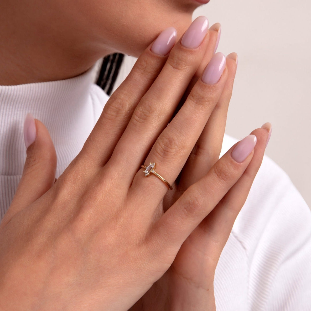 Elegant gold ring featuring a marquise-cut stone in a cross shape, showcased on a woman's hand with light pink manicured nails and a white turtleneck top, exuding refined charm.