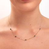 Model wearing a 14K gold plated minimalist necklace with evenly spaced navy blue crystals and gold hoop earrings

