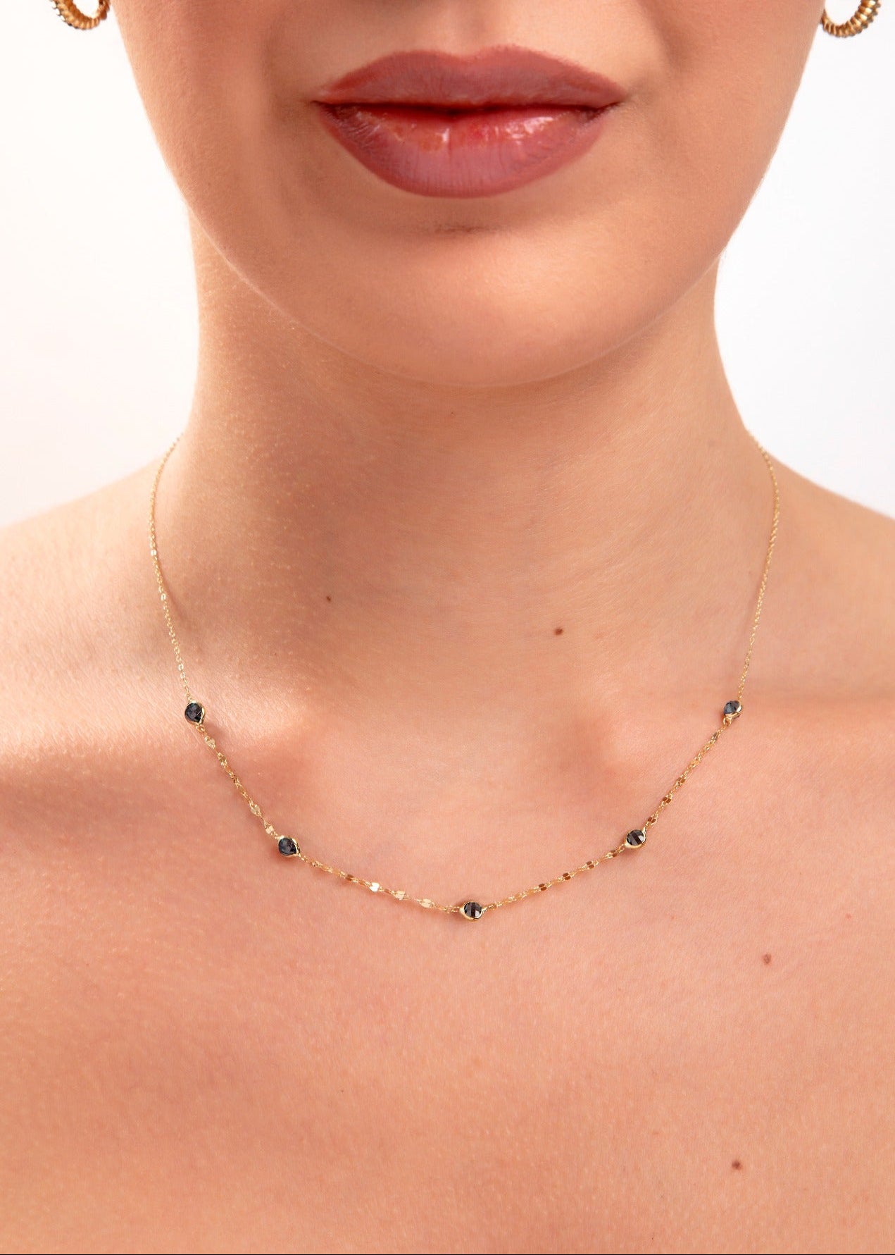 Model wearing a 14K gold plated minimalist necklace with evenly spaced navy blue crystals and gold hoop earrings

