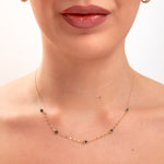 Model wearing a 14K gold plated minimalist necklace with evenly spaced navy blue crystals and gold hoop earrings

