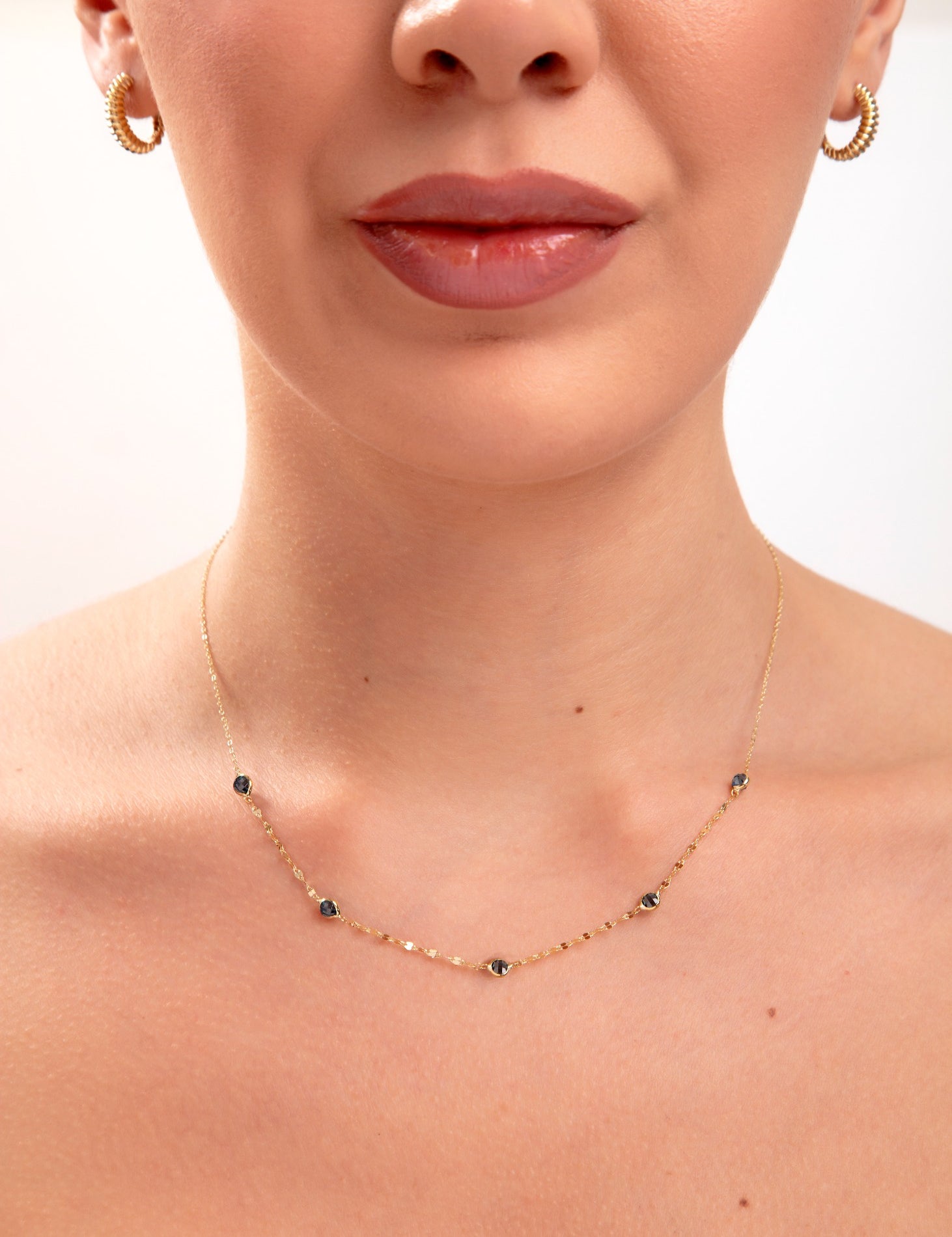 Model wearing a 14K gold plated minimalist necklace with evenly spaced navy blue crystals and gold hoop earrings

