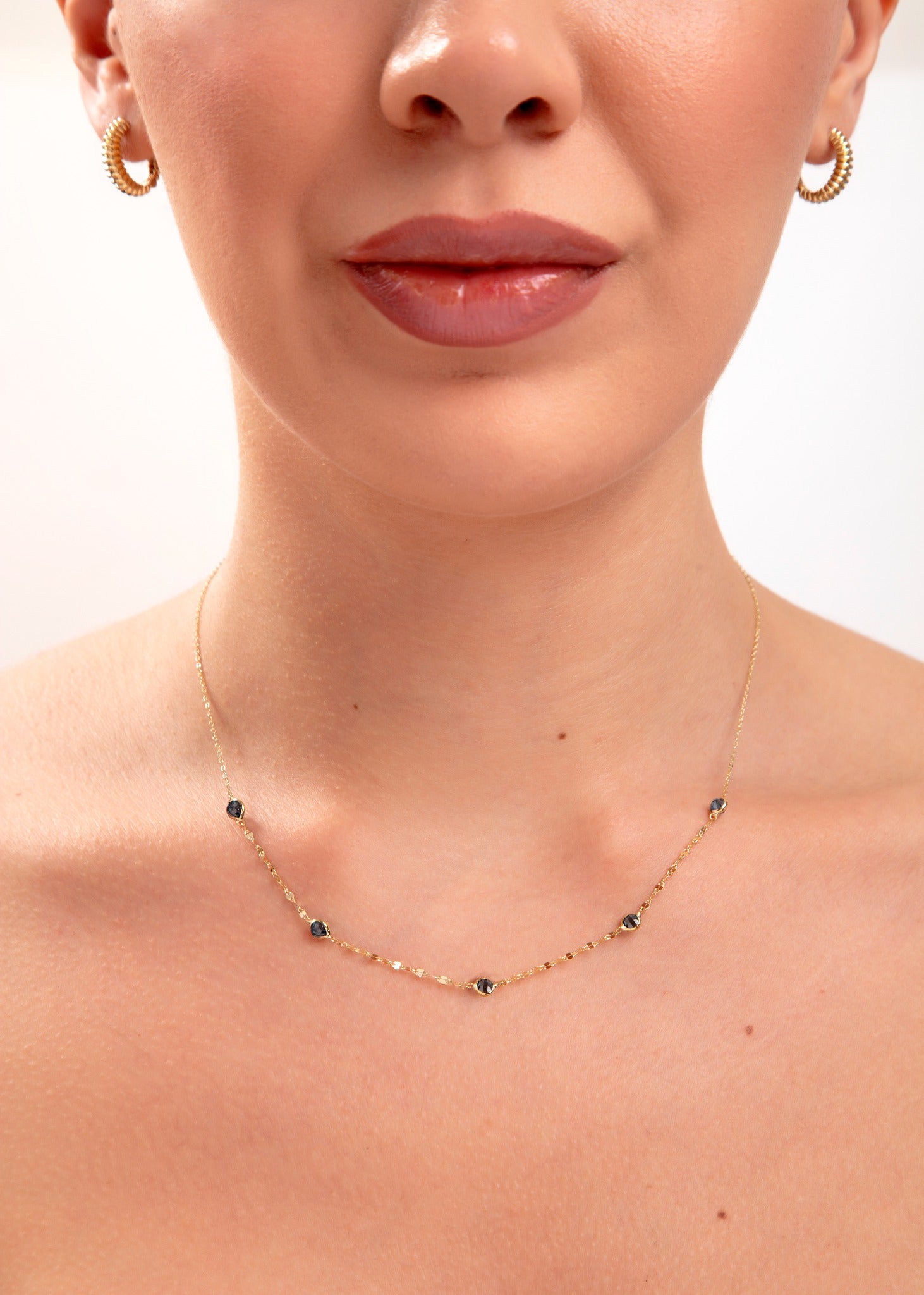 Model wearing a 14K gold plated minimalist necklace with evenly spaced navy blue crystals and gold hoop earrings

