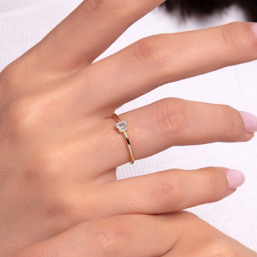 A dainty gold ring with a baguette-cut stone on a woman's hand, close-up view
