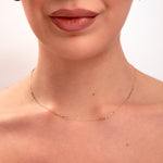 Close-up of minimalist gold paperclip chain necklace on model's neck, paired with small gold hoop earrings


