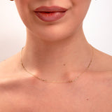 Close-up of minimalist gold paperclip chain necklace on model's neck, paired with small gold hoop earrings

