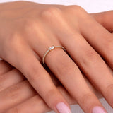 Woman's hand wearing a delicate gold ring featuring a center baguette cut stone and micro pavé band
