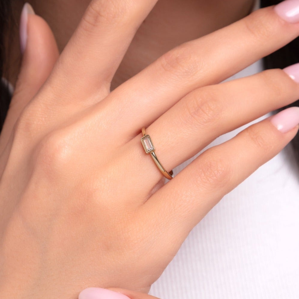 Close-up of a woman's hand wearing a minimalist baguette-cut diamond ring in 14K yellow gold – delicate and modern design.