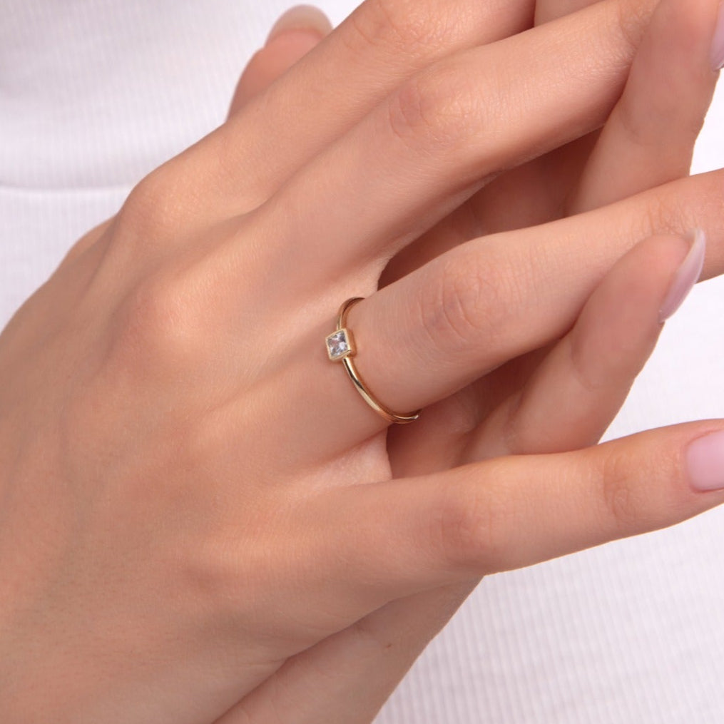 Minimalist princess cut solitaire ring in gold on a woman’s finger with pink manicure