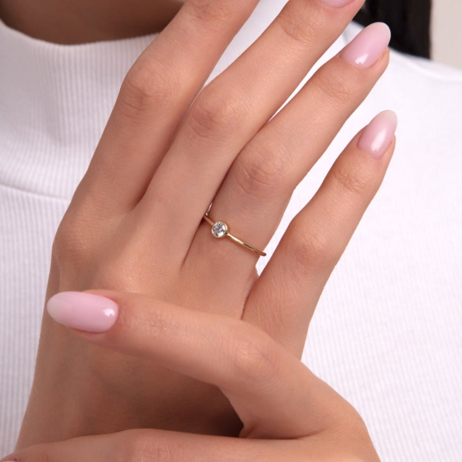 Minimalist round solitaire ring on woman's hand, featuring a dainty gold band and single stone