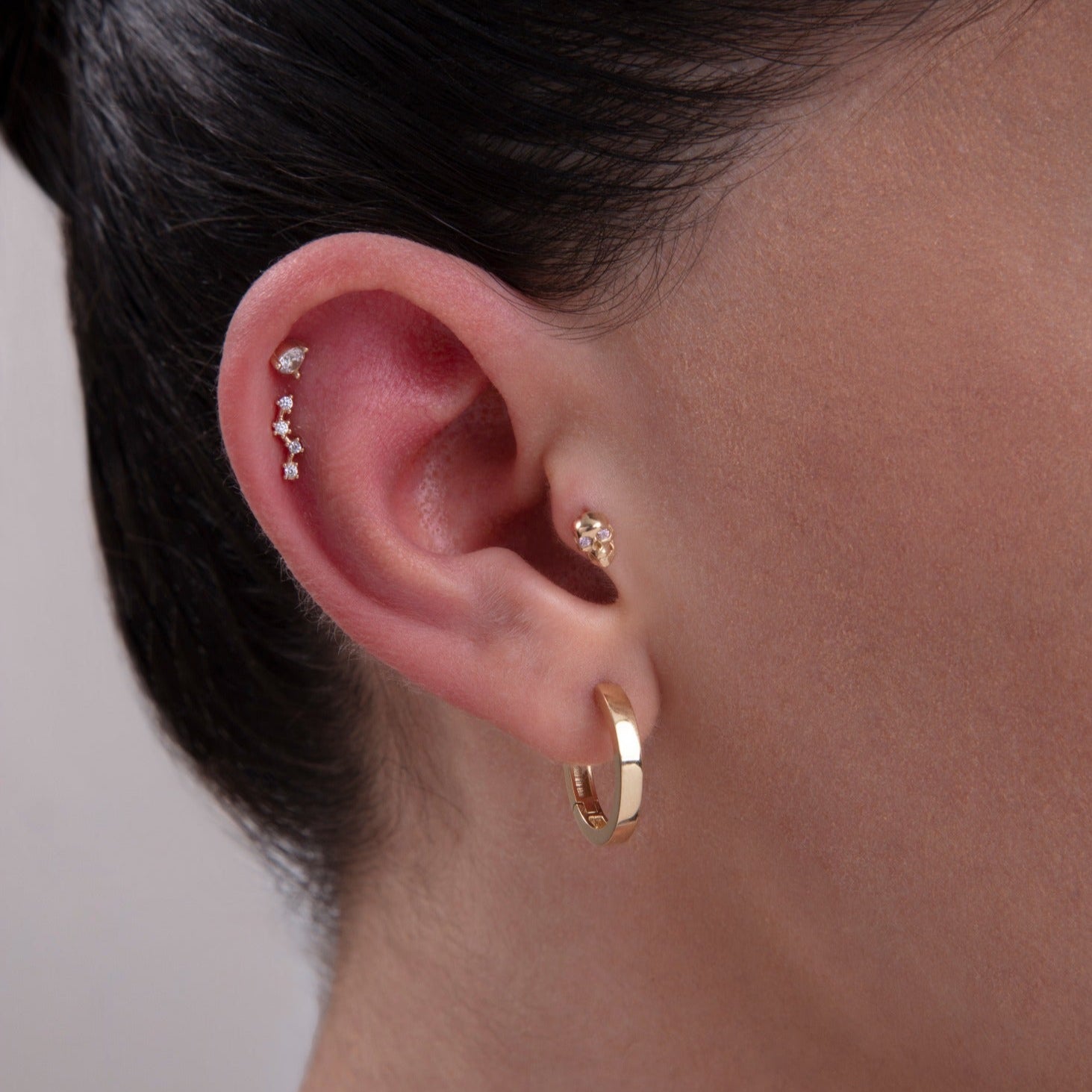 Model showcasing a curated ear stack featuring a teardrop CZ helix stud, constellation-inspired cartilage piercing, floral tragus stud, and classic gold hoop – a mix of elegant and modern 14K gold cartilage jewelry