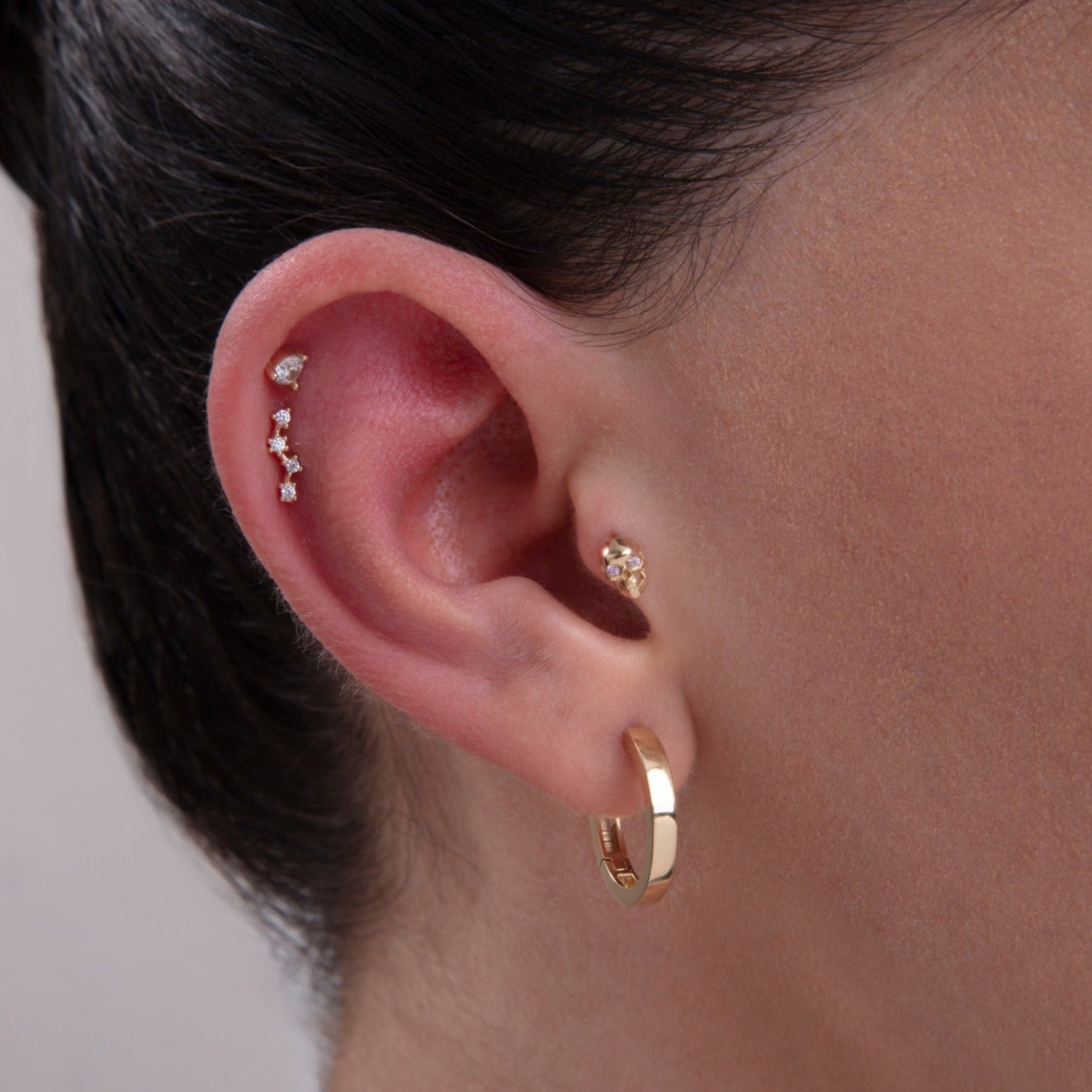 Model showcasing a curated ear stack featuring a teardrop CZ helix stud, constellation-inspired cartilage piercing, floral tragus stud, and classic gold hoop – a mix of elegant and modern 14K gold cartilage jewelry