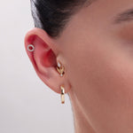 Model showcasing a layered ear stack with a 14K Gold Pavé Circle Helix Stud, a gold arrow-shaped cartilage earring with CZ accents, and a polished gold hoop in the lobe – A chic and symbolic curated ear combination