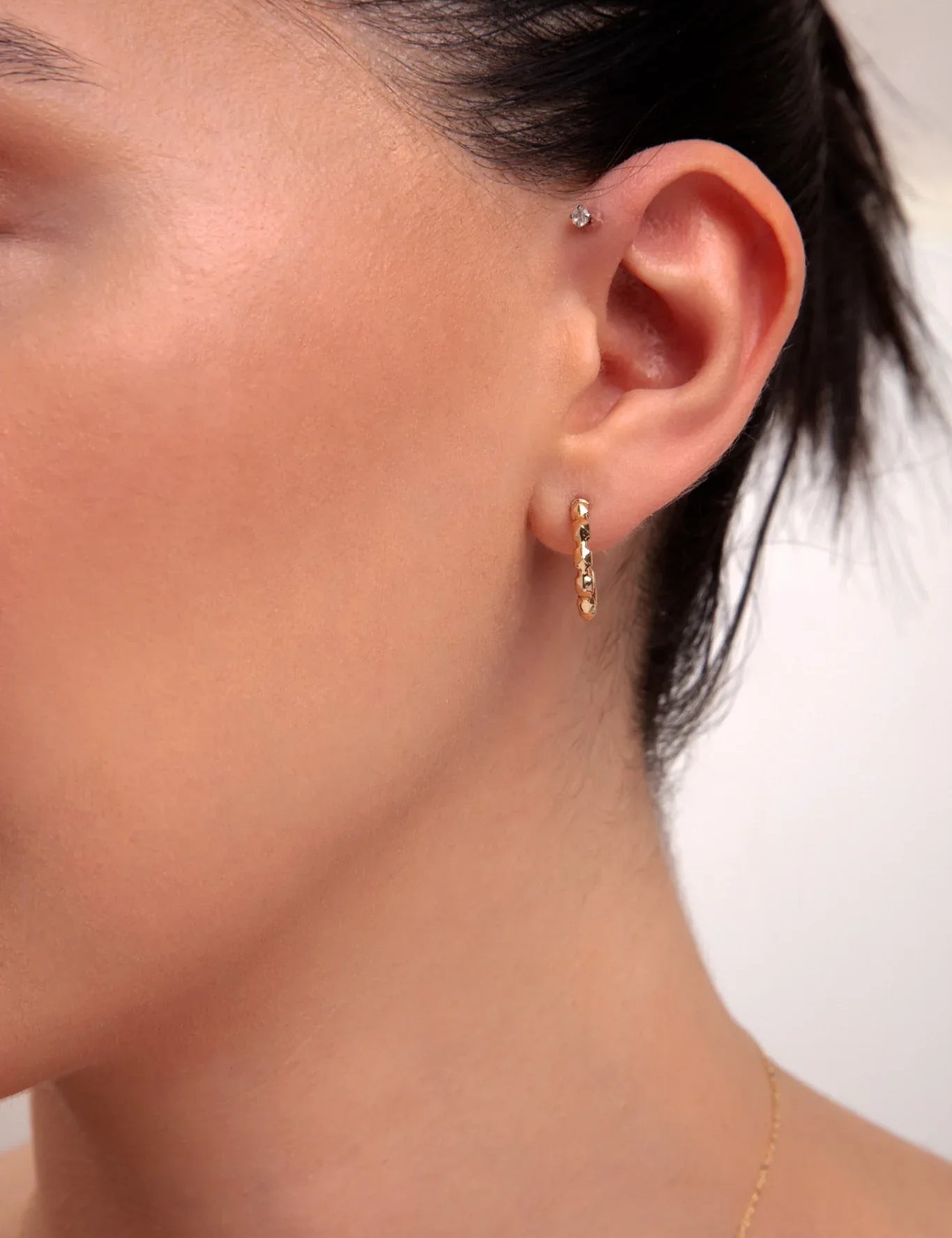 Model wearing mini gold faceted hoop earring

