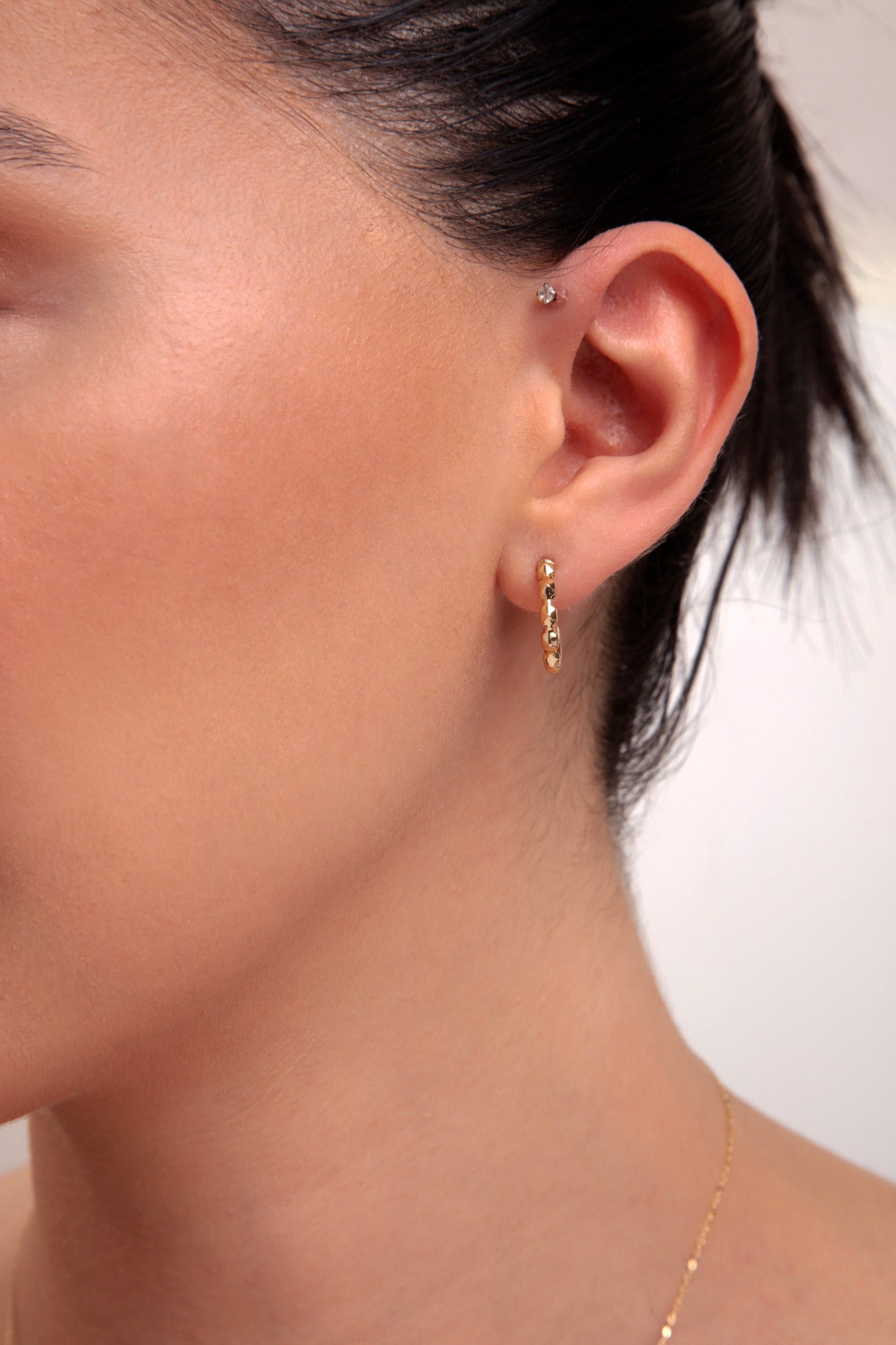 Model wearing mini gold faceted hoop earring

