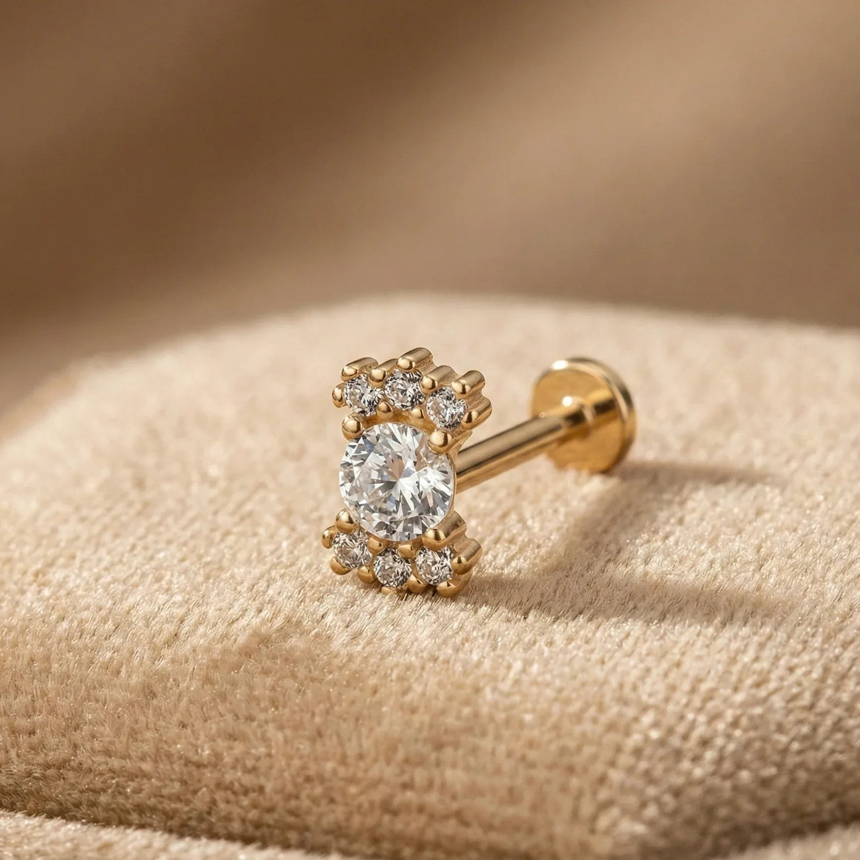 Gold earring with a diamond on a beige fabric background