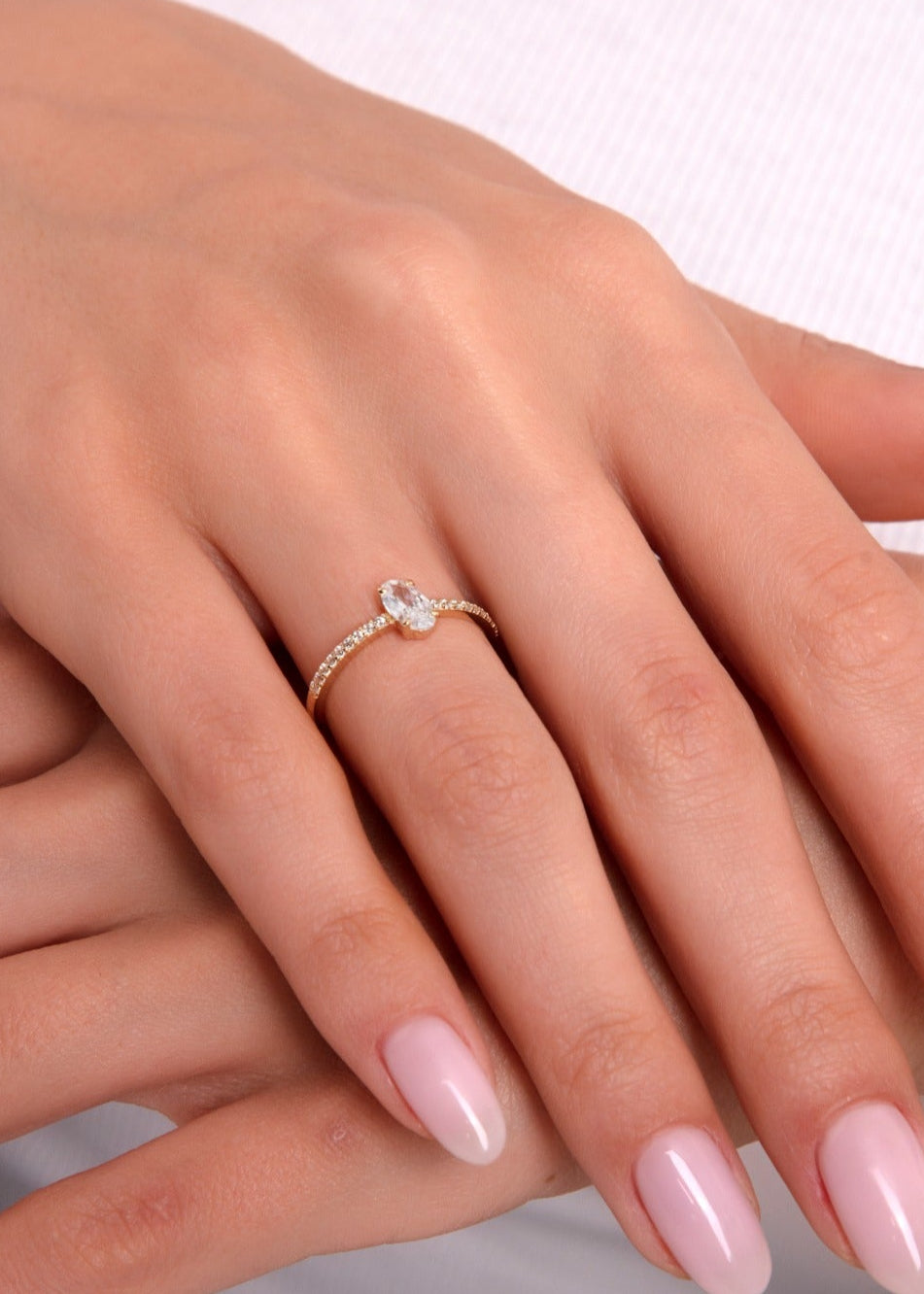 Teardrop-shaped solitaire gold ring with pavé band on a woman’s hand