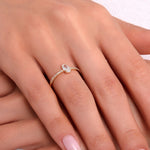 Teardrop-shaped solitaire gold ring with pavé band on a woman’s hand