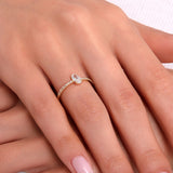 Teardrop-shaped solitaire gold ring with pavé band on a woman’s hand