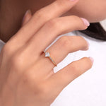 Woman wearing a princess cut gold ring with side stones, elegant hand pose in white outfit