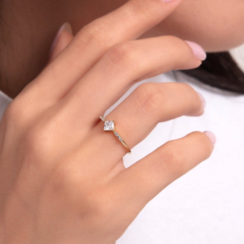 Woman wearing a princess cut gold ring with side stones, elegant hand pose in white outfit