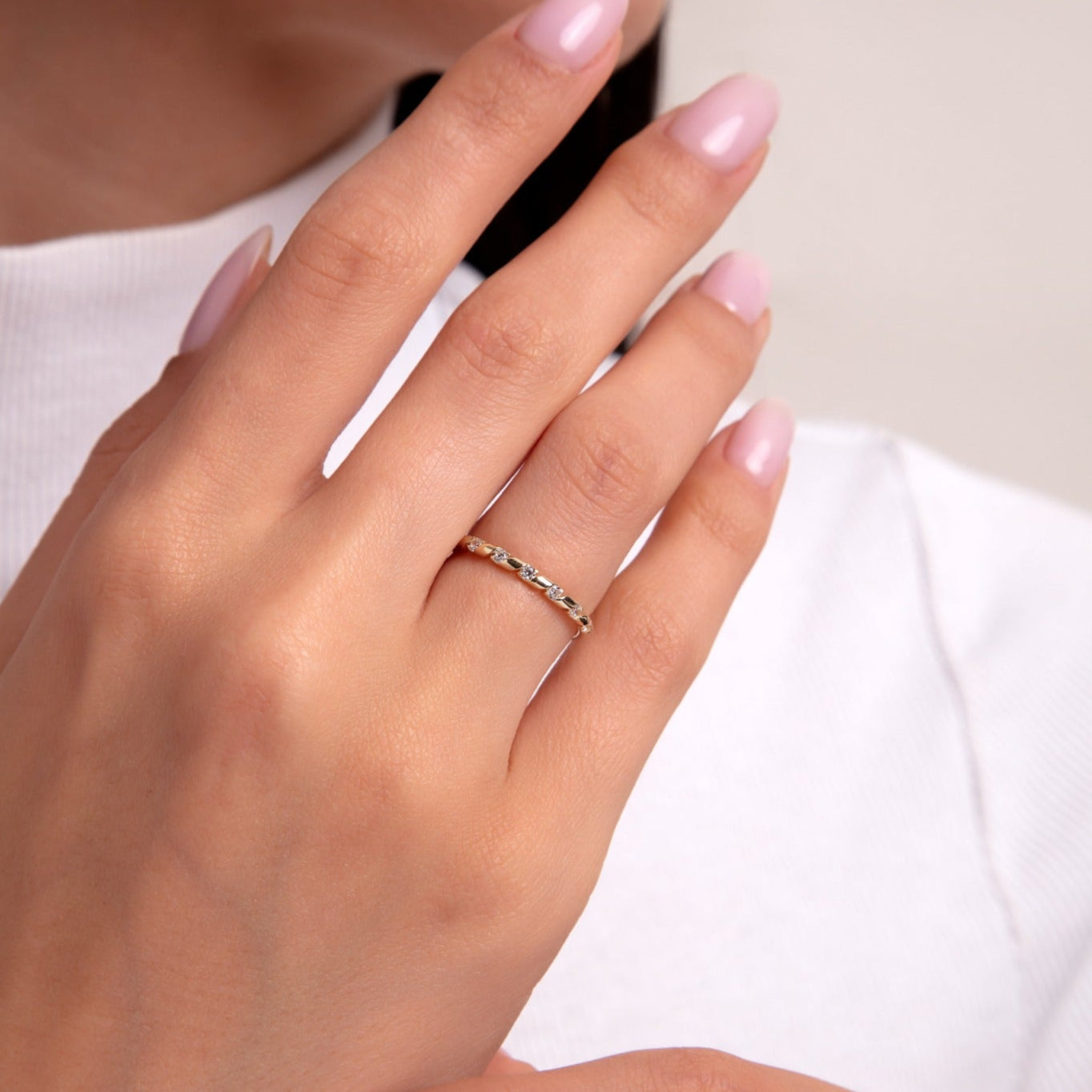 Minimal gold ring featuring alternating multicolor gemstones on a woman's hand