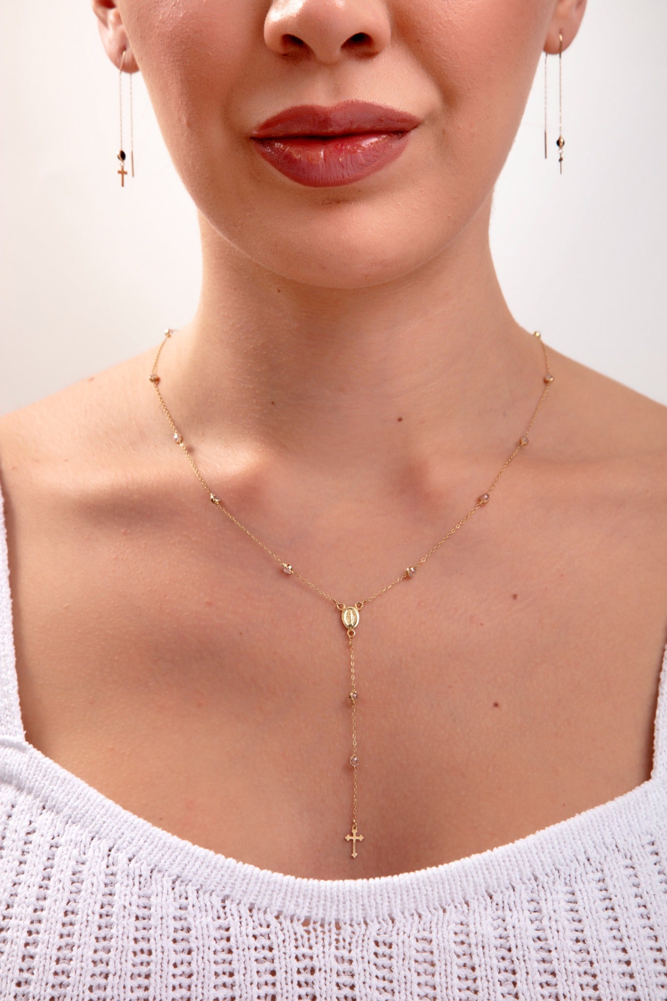 Model wearing a 14K gold plated rosary-style necklace with cross drop and Virgin Mary charm, plus matching threader earrings