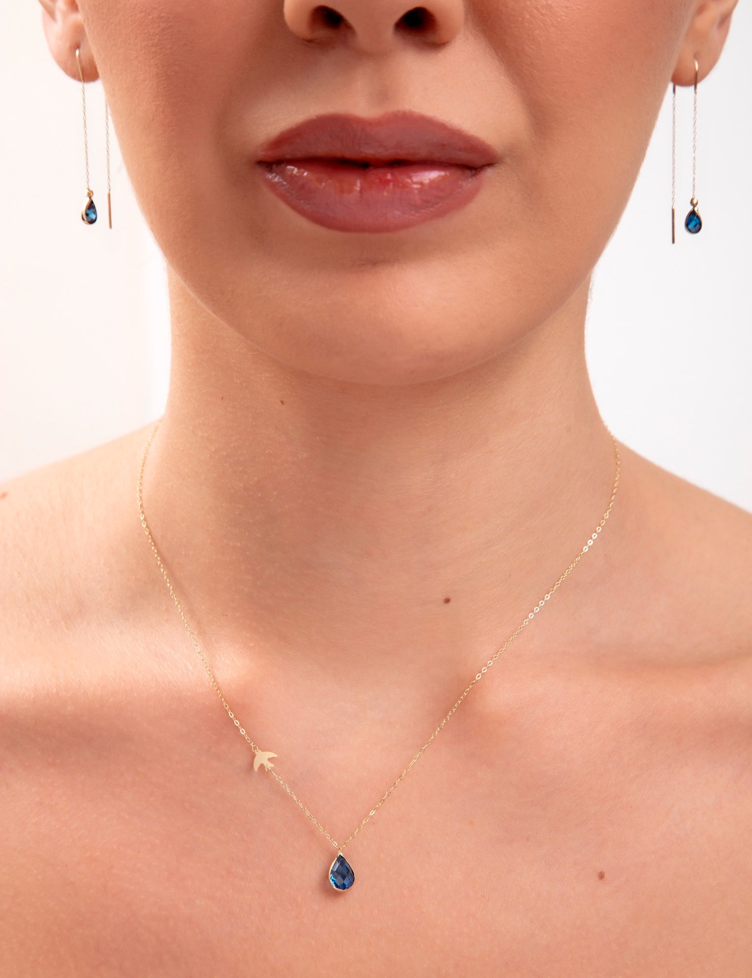 Model wearing a 14K gold plated teardrop sapphire necklace with bird charm and matching threader earrings

