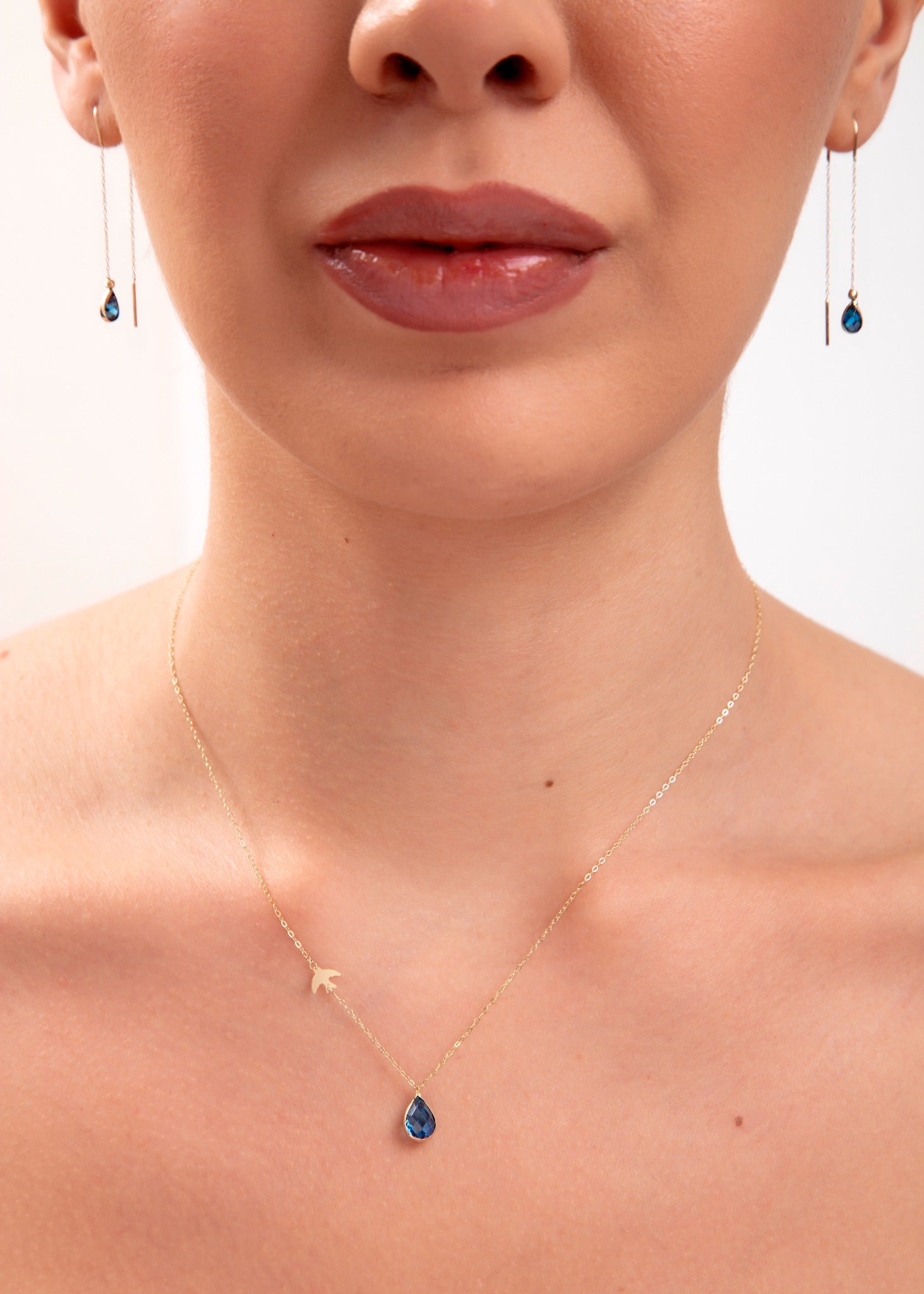 Model wearing a 14K gold plated teardrop sapphire necklace with bird charm and matching threader earrings

