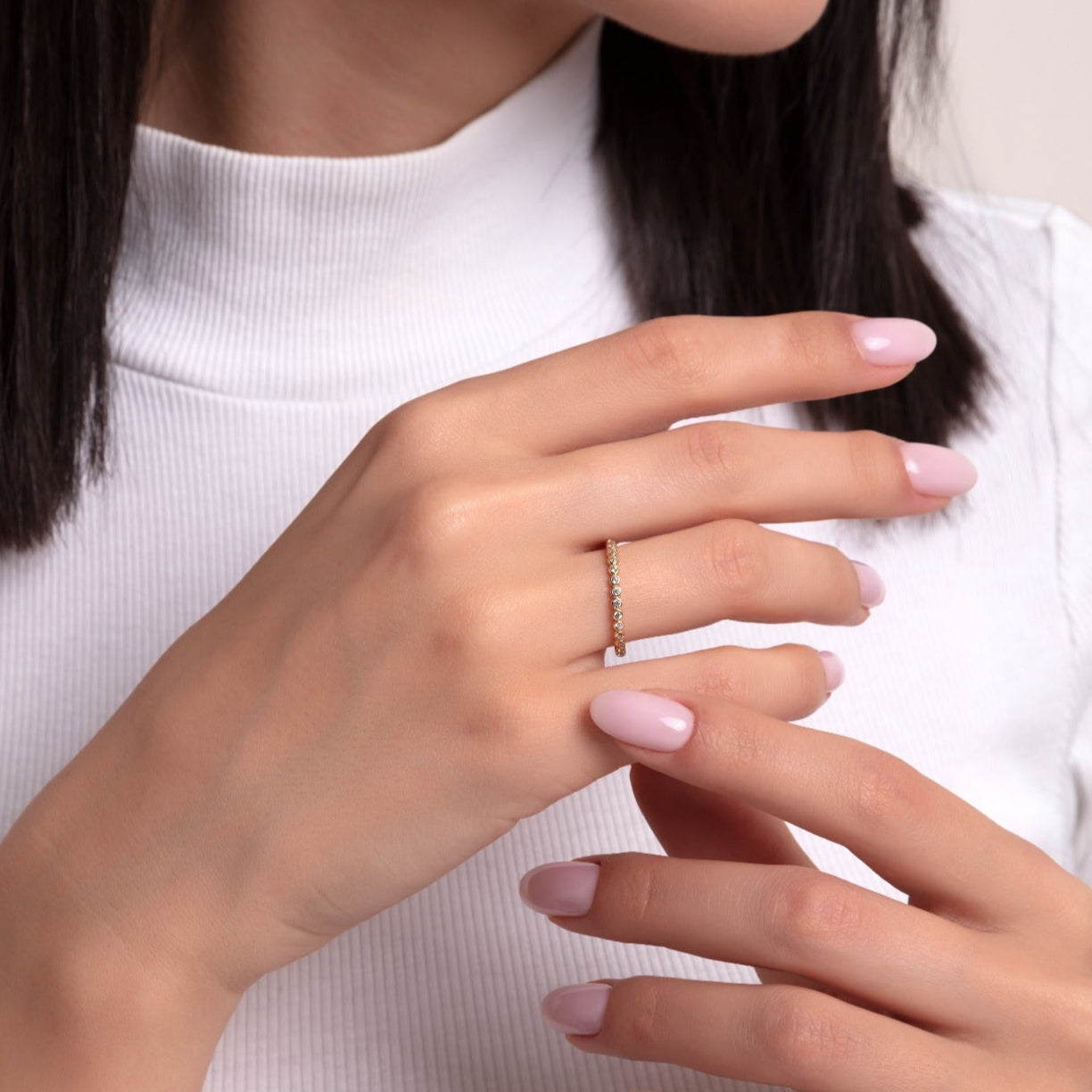 Minimalist gold eternity ring with tiny round-cut diamonds, worn by a woman with light pink nails in a close-up hand pose.

