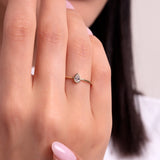 Close-up of a woman's hand wearing a delicate gold ring with a teardrop-shaped solitaire stone, styled with soft pink nails.