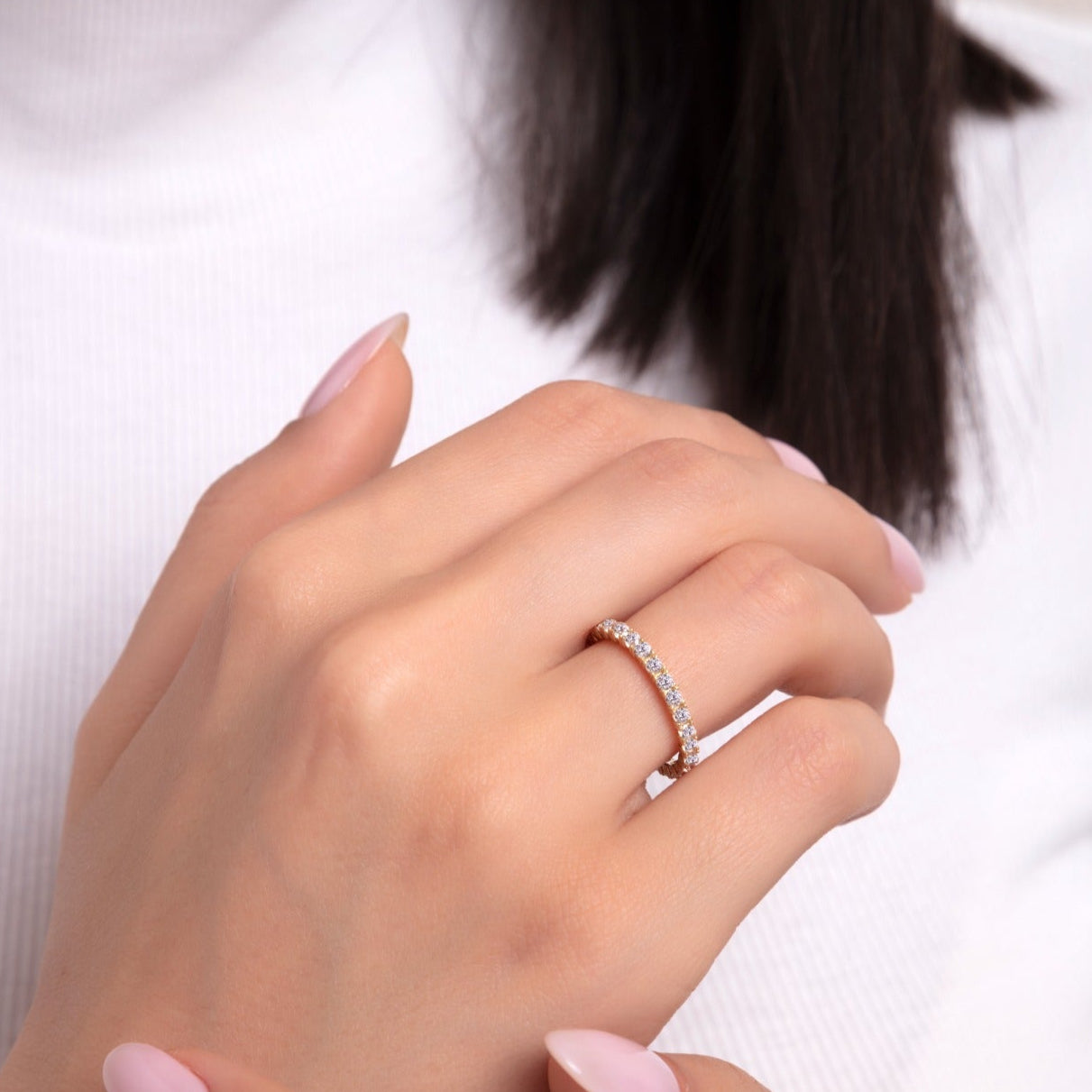 Rose gold eternity ring with a row of round cut sparkling stones, worn on a woman's hand with light pink manicure.

