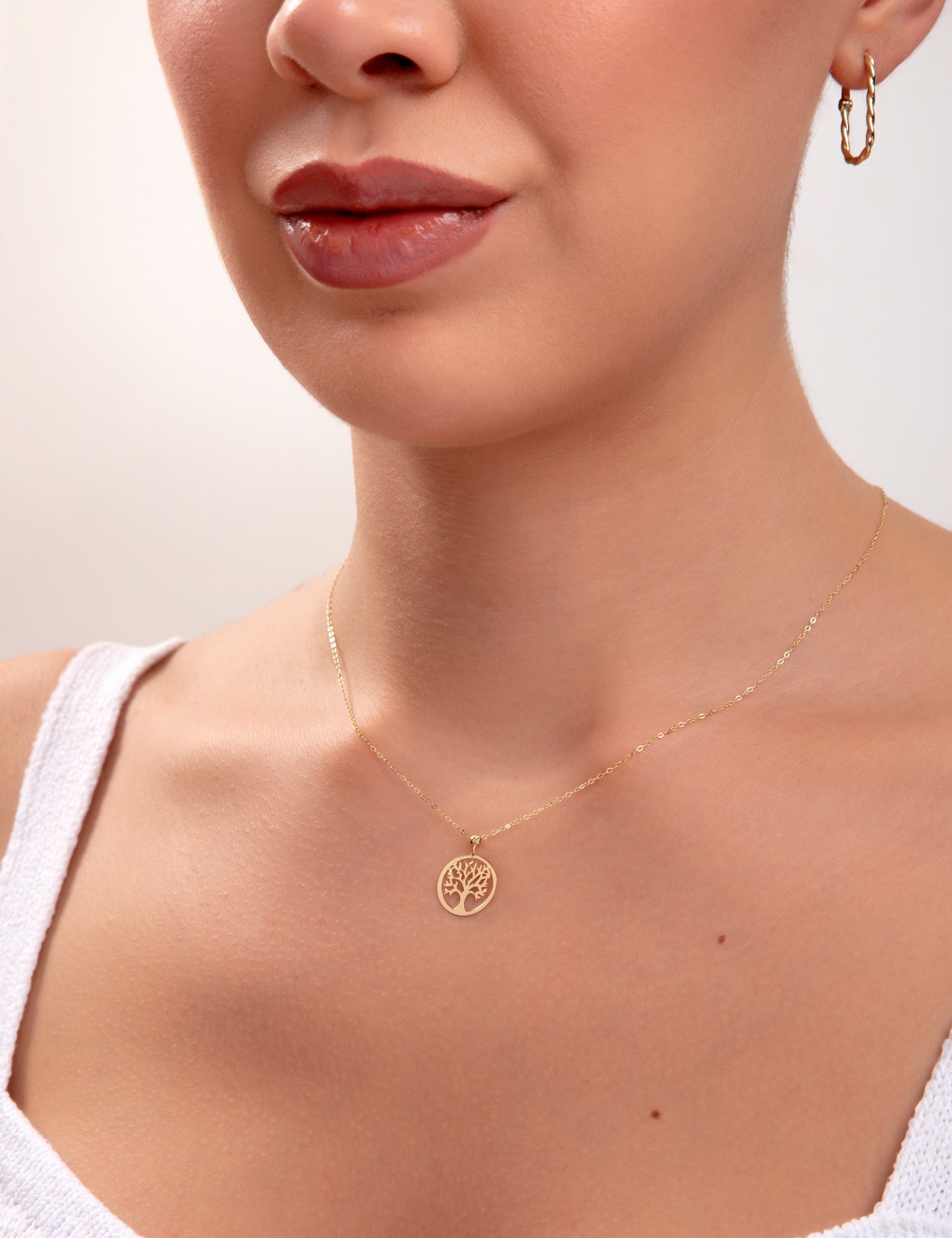 Model wearing a 14K gold plated Tree of Life pendant necklace with minimalist chain and gold hoop earrings

