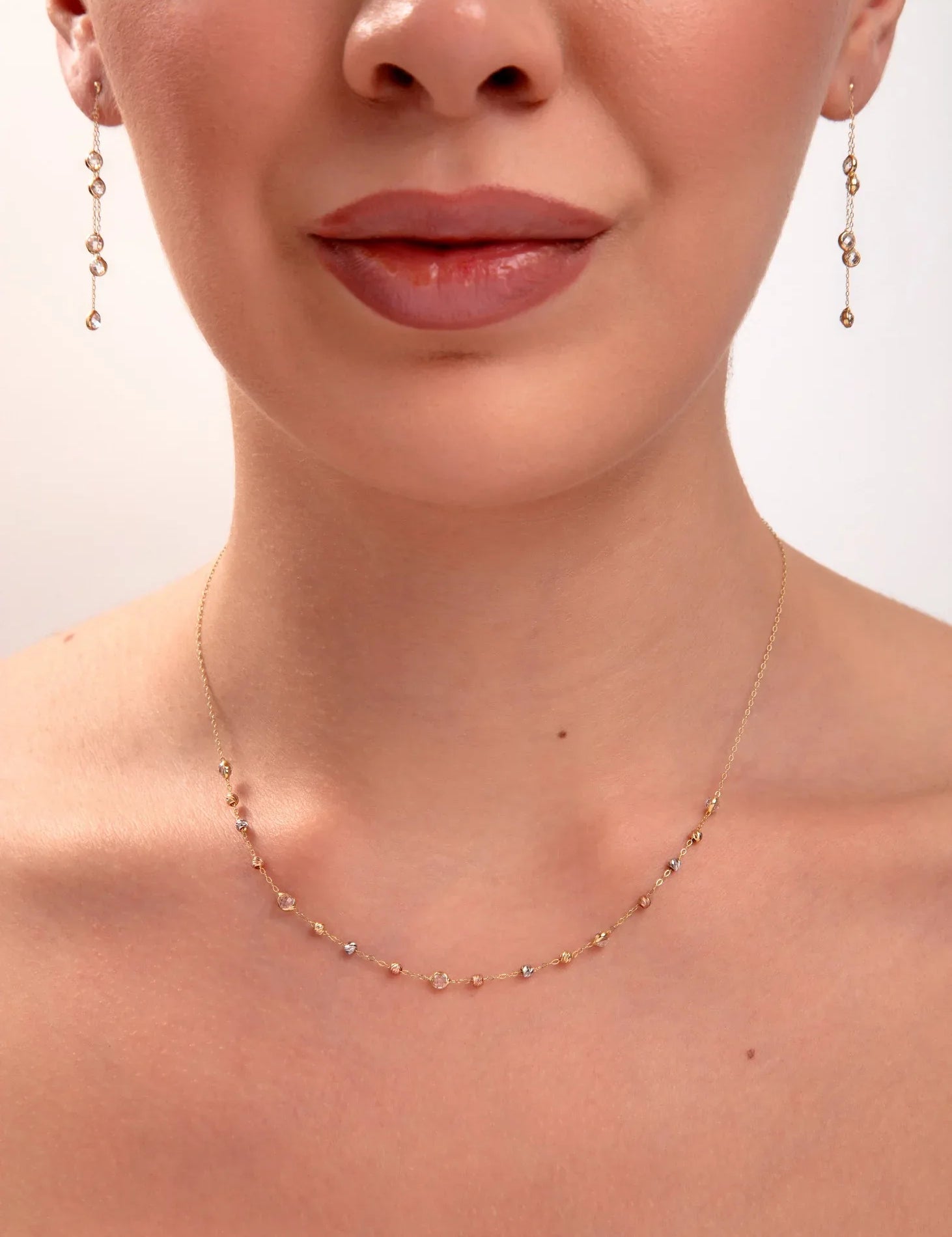 Close-up of a woman wearing a delicate necklace and earrings on a plain background