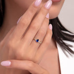Woman’s hand wearing a 14K gold chain band ring with a bold pear-cut sapphire blue stone, showcasing a luxurious and confident style.
