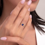 Woman’s hand wearing a 14K gold chain band ring with a bold pear-cut sapphire blue stone, showcasing a luxurious and confident style.