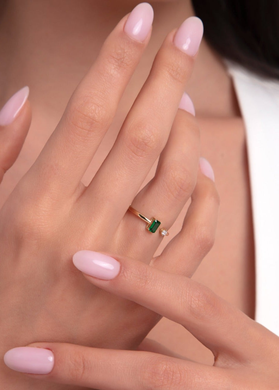 Woman showcasing an open 14K gold ring with baguette-cut green emerald and a diamond accent