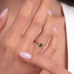 Woman showcasing an open 14K gold ring with baguette-cut green emerald and a diamond accent