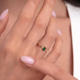 Woman showcasing an open 14K gold ring with baguette-cut green emerald and a diamond accent