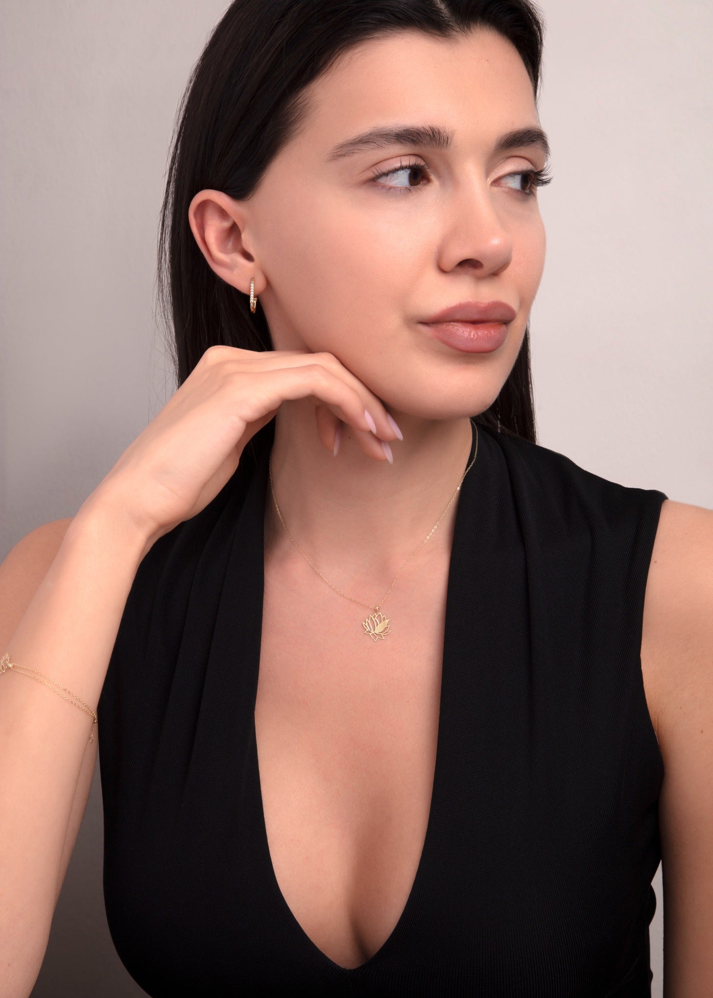 Woman wearing a 14K gold lotus flower pendant necklace styled with a deep V-neck black dress, showcasing an elegant and spiritual look.