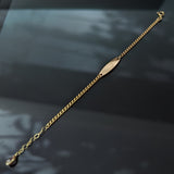 14K gold baby ID bracelet for girls with a blank nameplate and pink gemstone charm, displayed on a black background